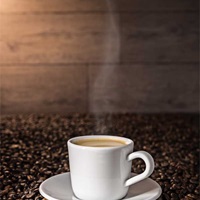 Objektfoto von dampfender Tasse Kaffee (Expresso) auf Kaffeebohnen